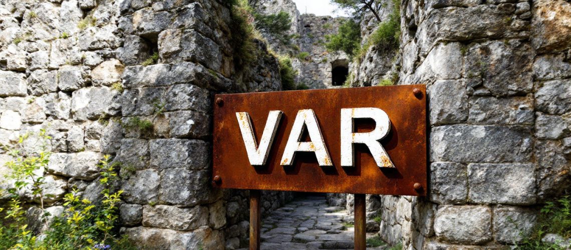 Variscan Mines Ltd-VAR-Rusty sign with "VAR" in front of ancient stone ruins and greenery.